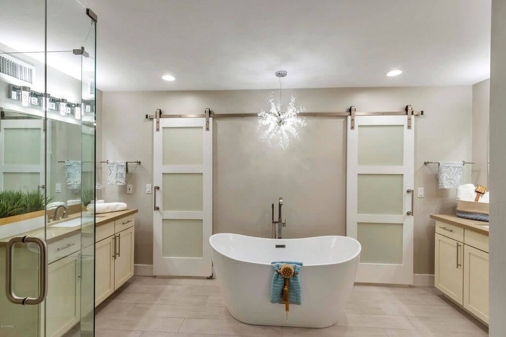 A modern, minimalist bathroom featuring a freestanding bathtub with elegant lighting and glass sliding doors.