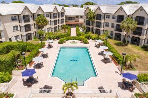 Aerial view of a hotel with a central swimming pool surrounded by buildings and greenery.