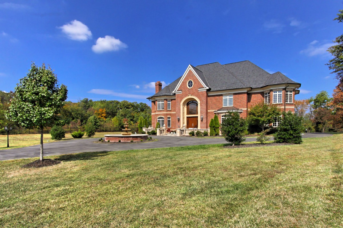 A large brick mansion with a spacious lawn under a clear blue sky.