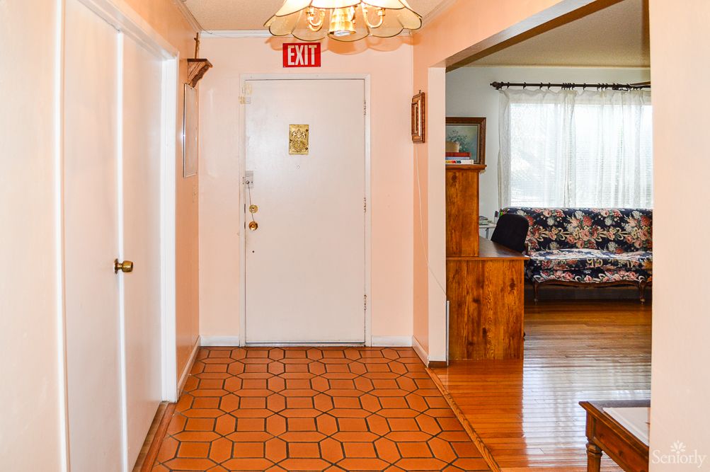 A hallway leading to a front door, featuring wooden flooring and a ceiling light.