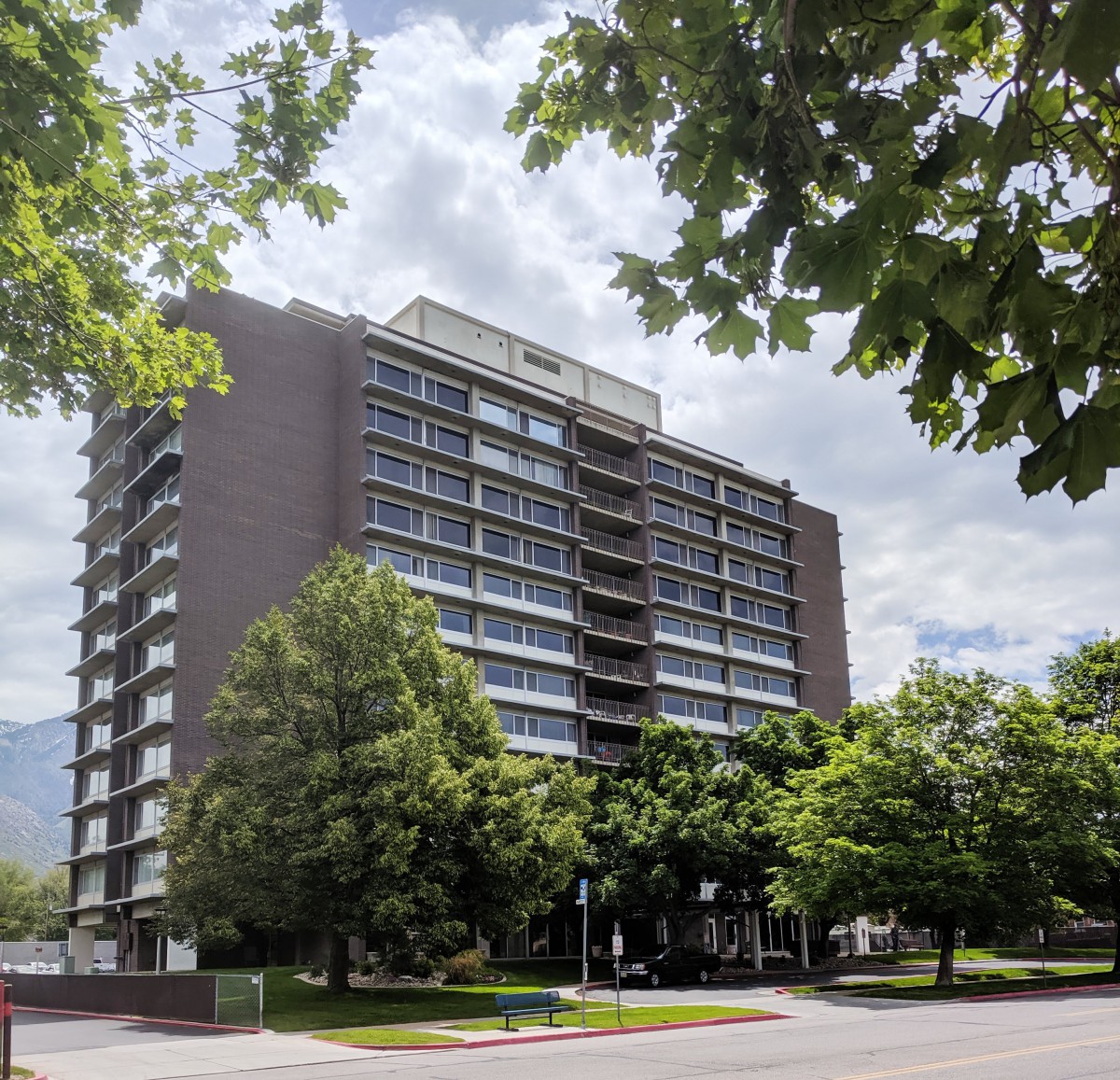 A high-rise building surrounded by trees under a partly cloudy sky.