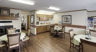 A cozy dining area with a small kitchen, featuring wooden floors and several tables with chairs.