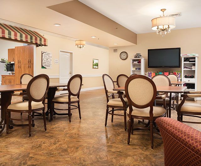 A cozy dining area with round tables and elegant chairs, featuring a television and decorative light fixtures.