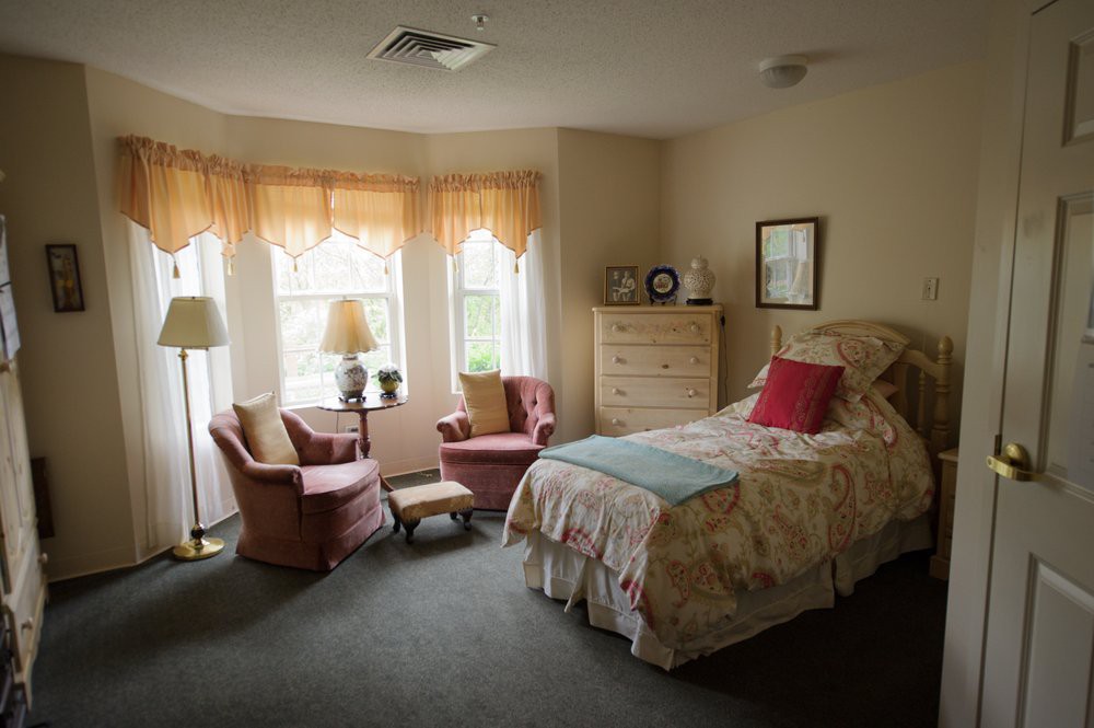 A cozy bedroom with a single bed, two armchairs by a window, and soft lighting.