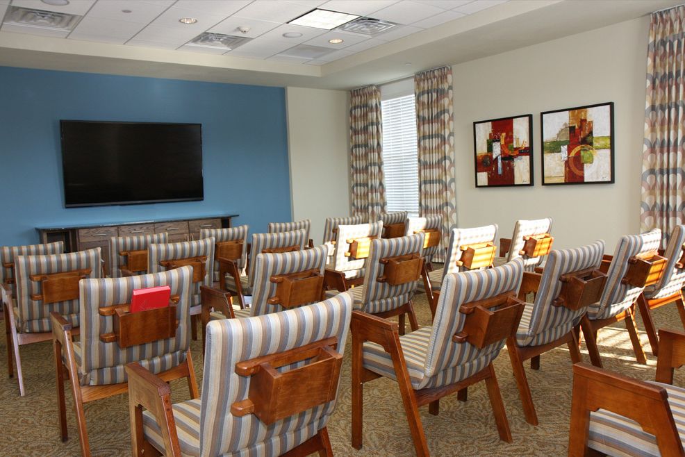 A modern conference room with neatly arranged chairs and a large television on the wall.