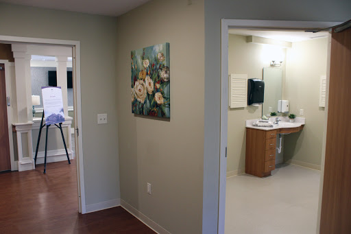 A view of a hallway in a medical facility, featuring a floral painting on the wall and an entrance to a bathroom.