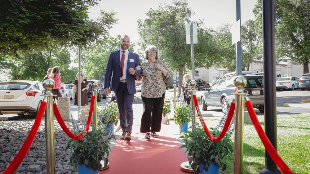 A man and a woman walk down a red carpet at an outdoor event.