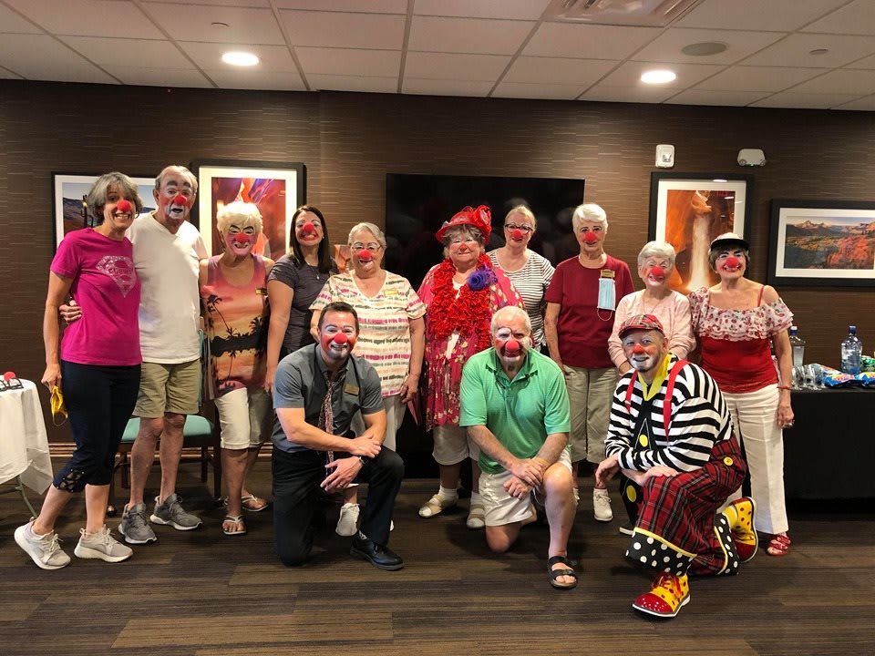 A group of adults dressed in funny costumes and clown outfits gathered indoors for a fun event.