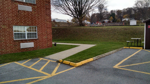 A view of a sidewalk adjacent to a brick building, leading through a grassy area with a tree in the background.