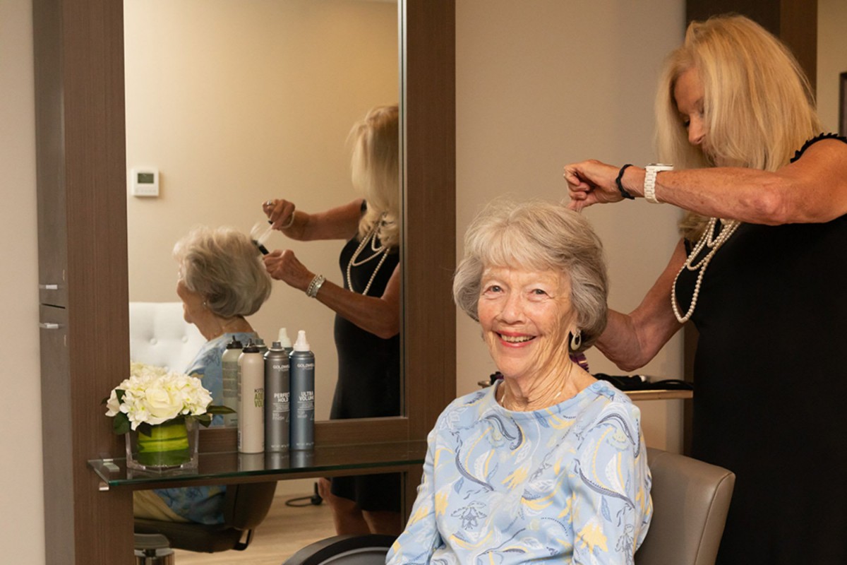 An elderly woman smiling while getting her hair styled in a salon.