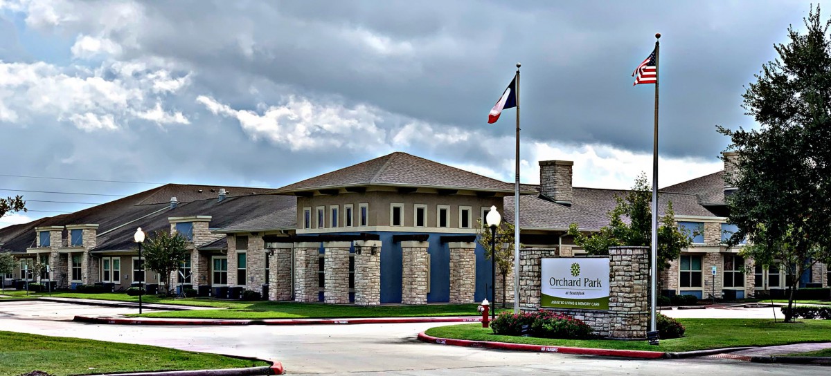 A modern building under a cloudy sky with a flag and signage at the entrance.