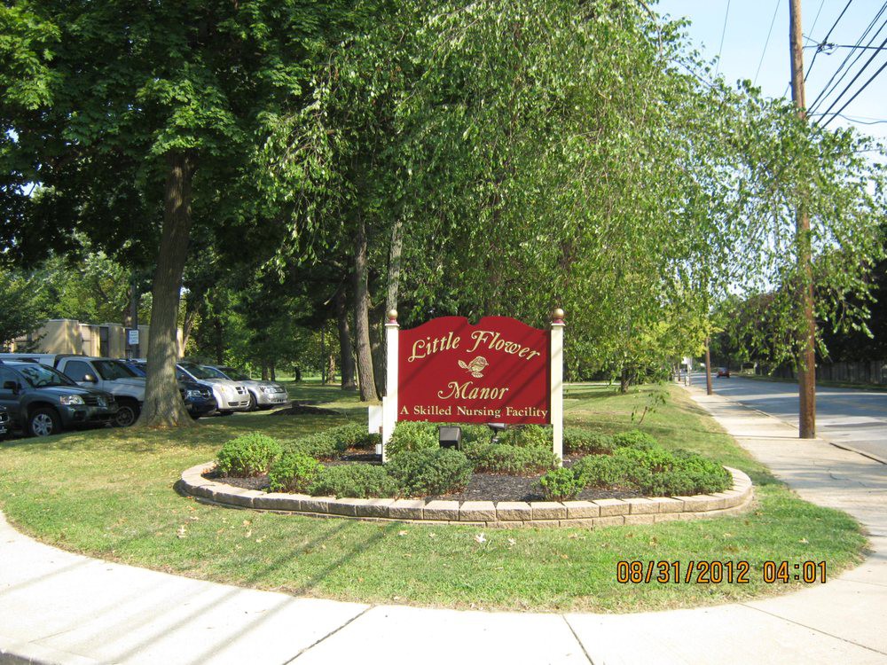 A decorative sign surrounded by landscaped greenery near a roadside.