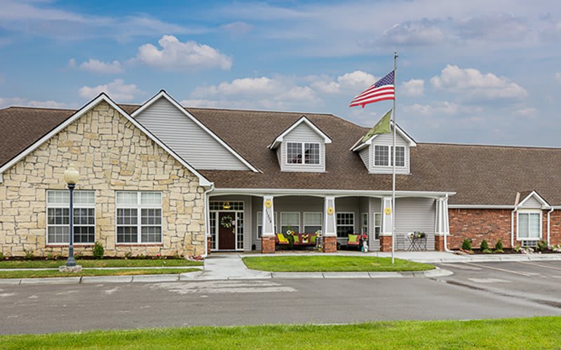 A charming house with an American flag flying, surrounded by a green lawn under a partly cloudy sky.