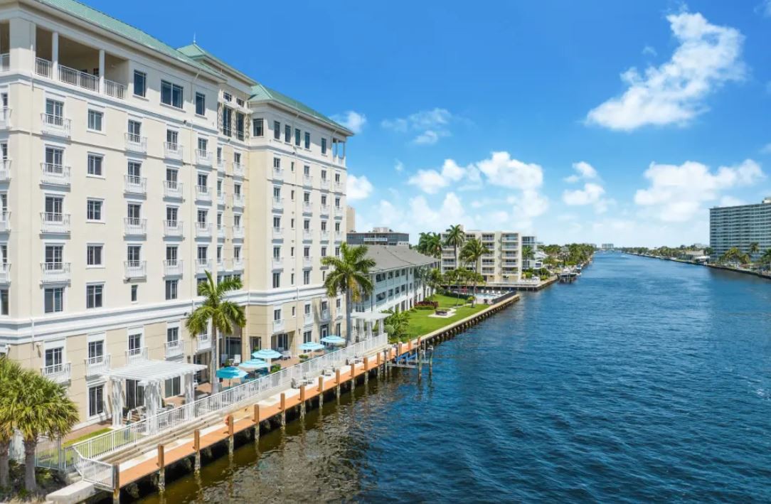 A beautiful waterfront hotel with palm trees and a scenic view of the river on a sunny day.