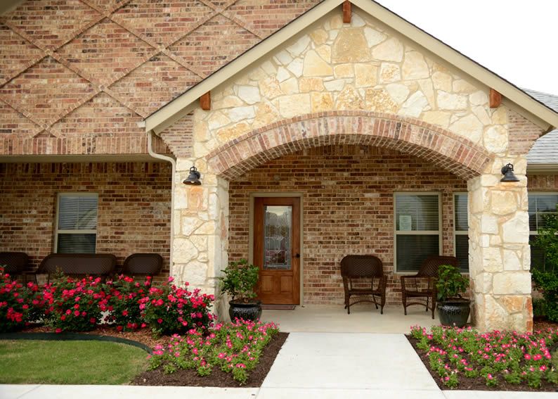 A welcoming front porch with a brick and stone exterior, adorned with flowers and seating.