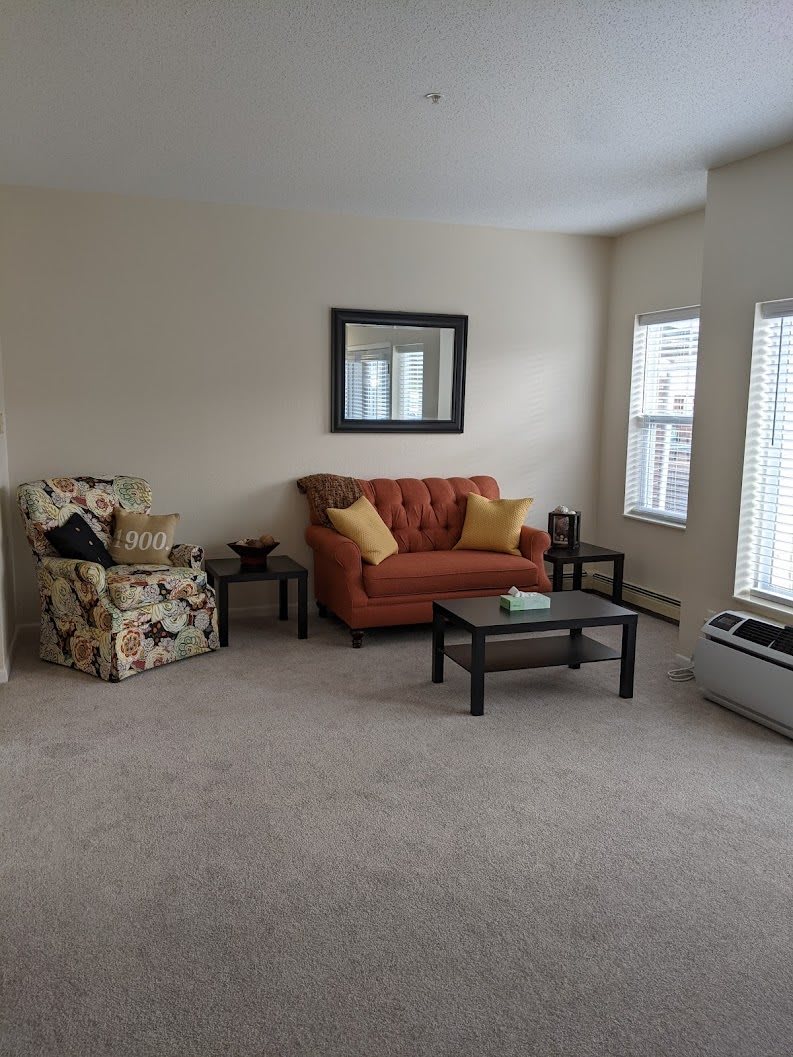 A cozy living room with a sofa, armchair, coffee table, and large windows.