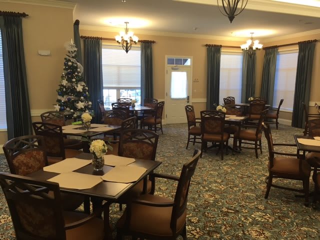 A cozy dining room with tables and chairs, decorated for the holidays with a Christmas tree.