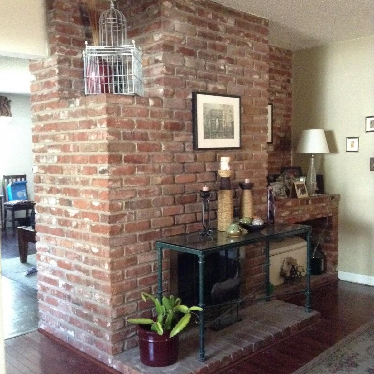 A cozy living space featuring a prominent brick wall and fireplace, adorned with plants and artwork.