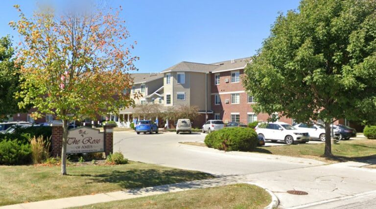 A suburban apartment building with a parking lot and trees in the foreground.