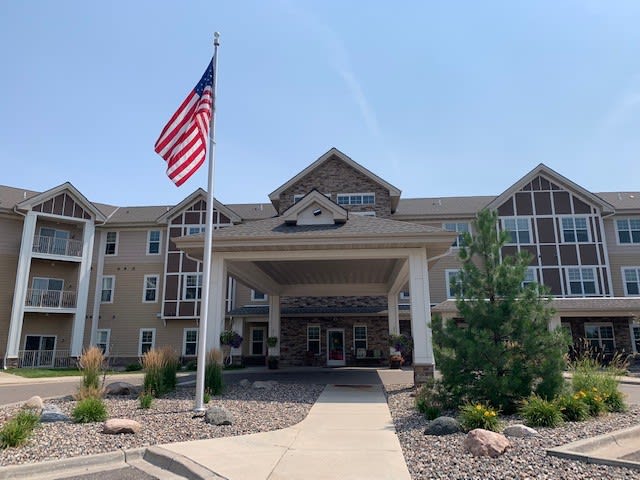 The image shows the entrance of a building with an American flag and well-maintained landscaping.