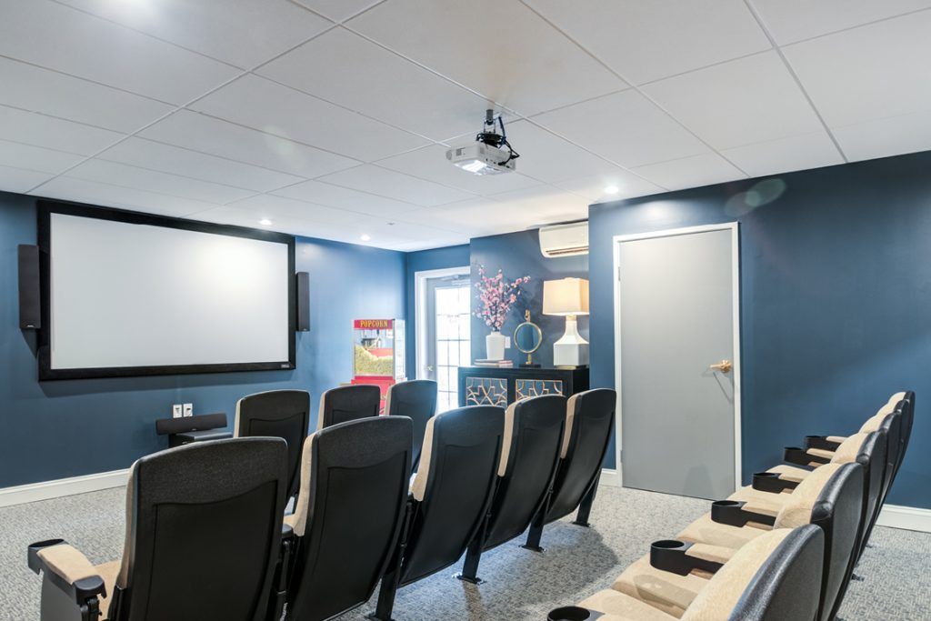 A small home theater room featuring multiple chairs, a large screen, and a ceiling-mounted projector set against blue walls.