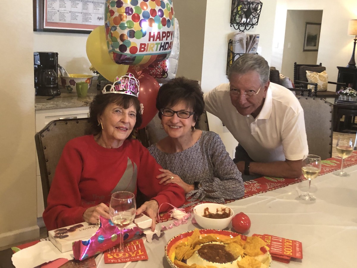 A joyful birthday celebration with family members gathered around a table with a cake and balloons.