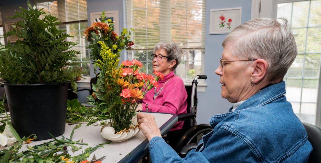 Two elderly individuals participate in a flower arranging activity at a care center.
