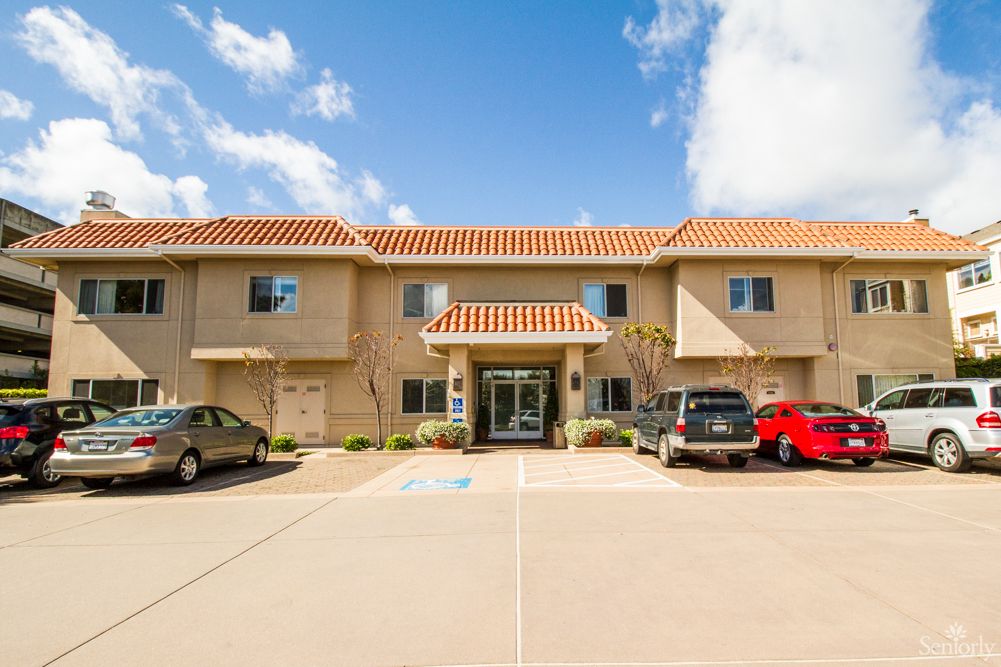 A two-story apartment building with cars parked in front on a sunny day.