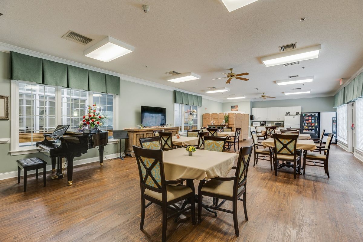 A spacious dining area with neatly arranged tables and chairs, featuring a piano and ceiling fans.