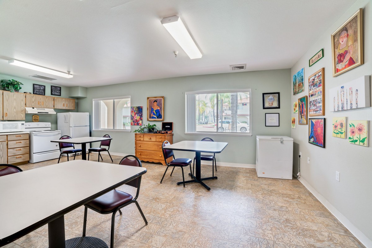 A community room with tables, chairs, and artwork on the walls.