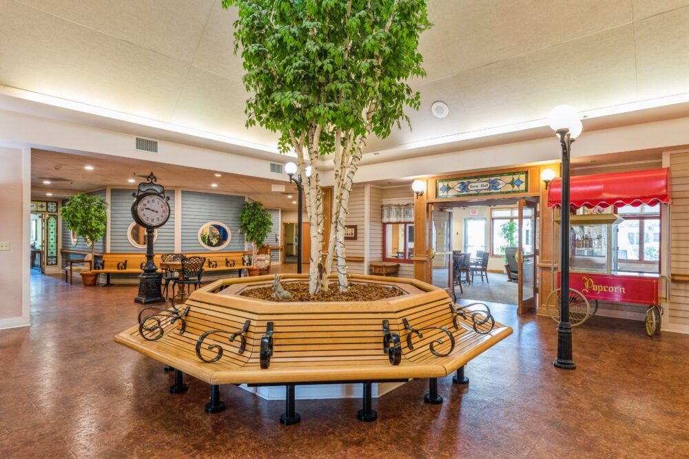 A modern lobby features a central tree surrounded by a circular bench, with a vintage-style clock adding to the decor.