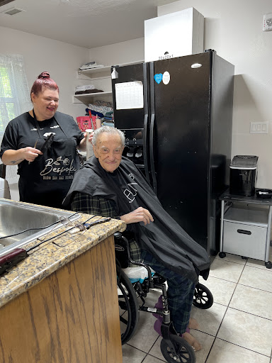 A caregiver is giving a haircut to a senior citizen in a cozy indoor setting.