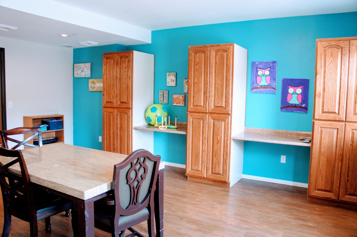 A colorful room with wooden furniture, including a table and chairs, cabinets, and artwork on the walls.