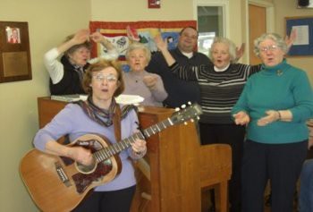 A group of elderly people singing along with a guitar player.