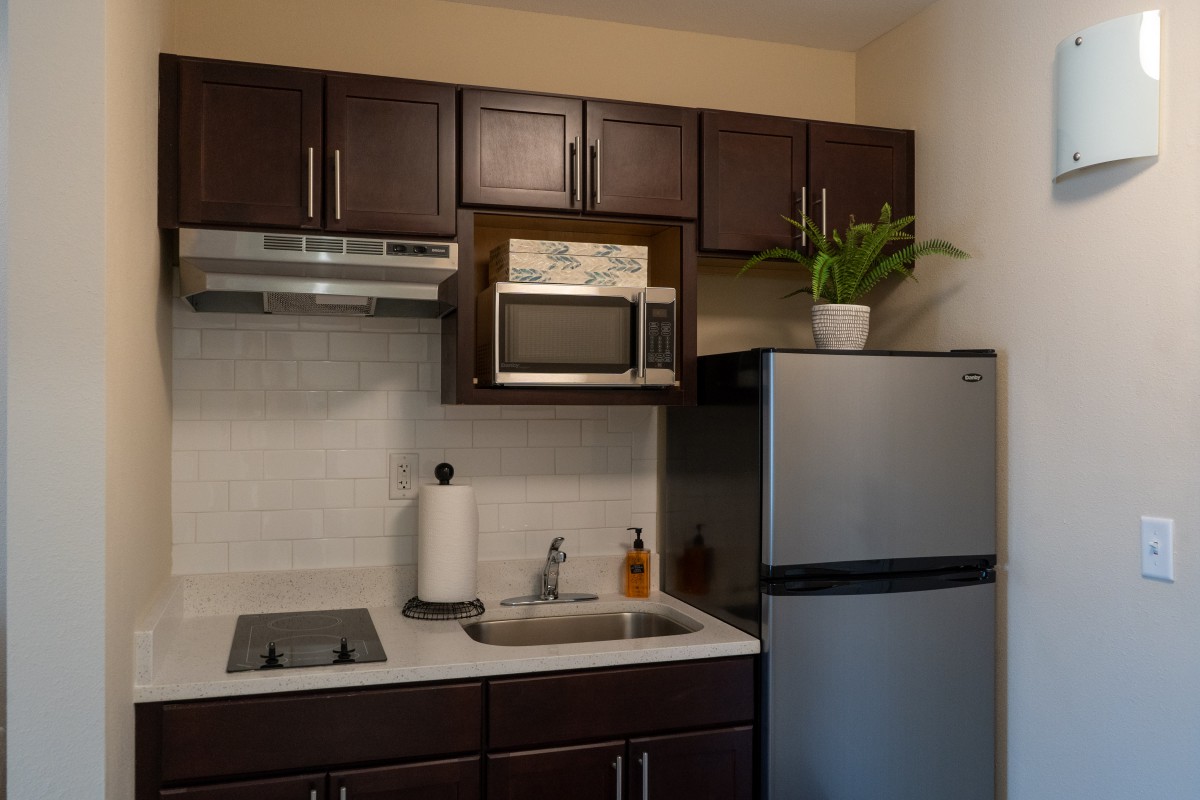 A compact modern kitchen with dark cabinets, a microwave, refrigerator, and a small cooktop.