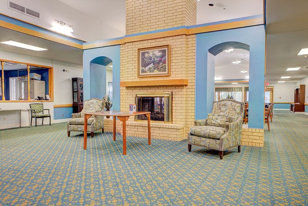 A cozy lobby with a fireplace surrounded by armchairs and a table, featuring warm decor.