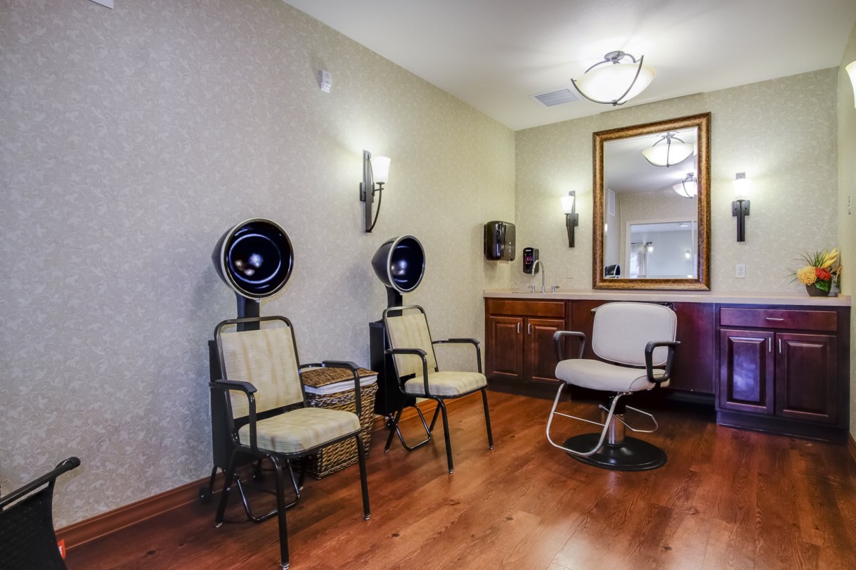 A cozy salon interior featuring hair drying stations with chairs, a large mirror, and warm lighting.