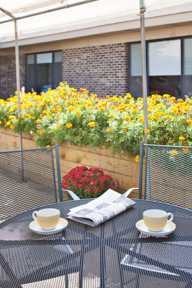 A cozy patio setting with two tea cups, a newspaper on the table, and colorful flowers in the background.