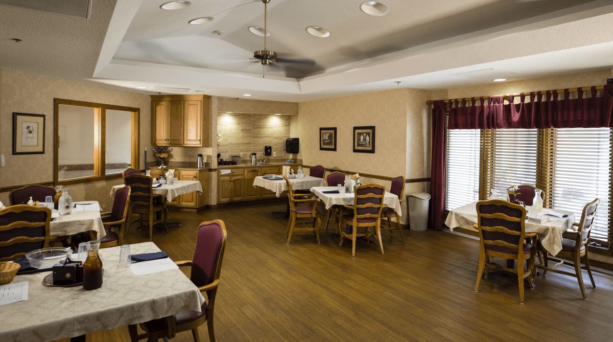A cozy dining room with tables and chairs, adjacent to a small kitchen area.
