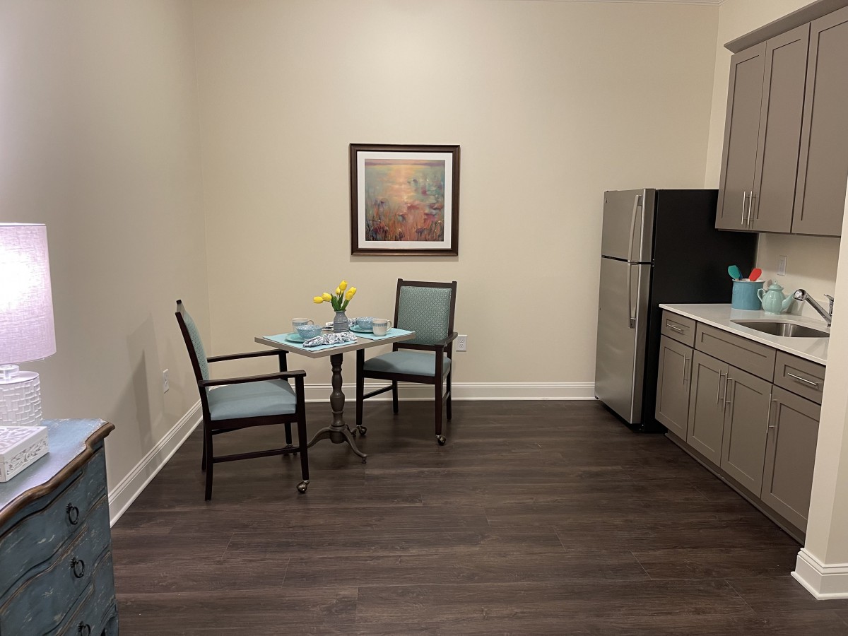 A small kitchen with a dining area, featuring a table set for two next to a refrigerator and artwork on the wall.