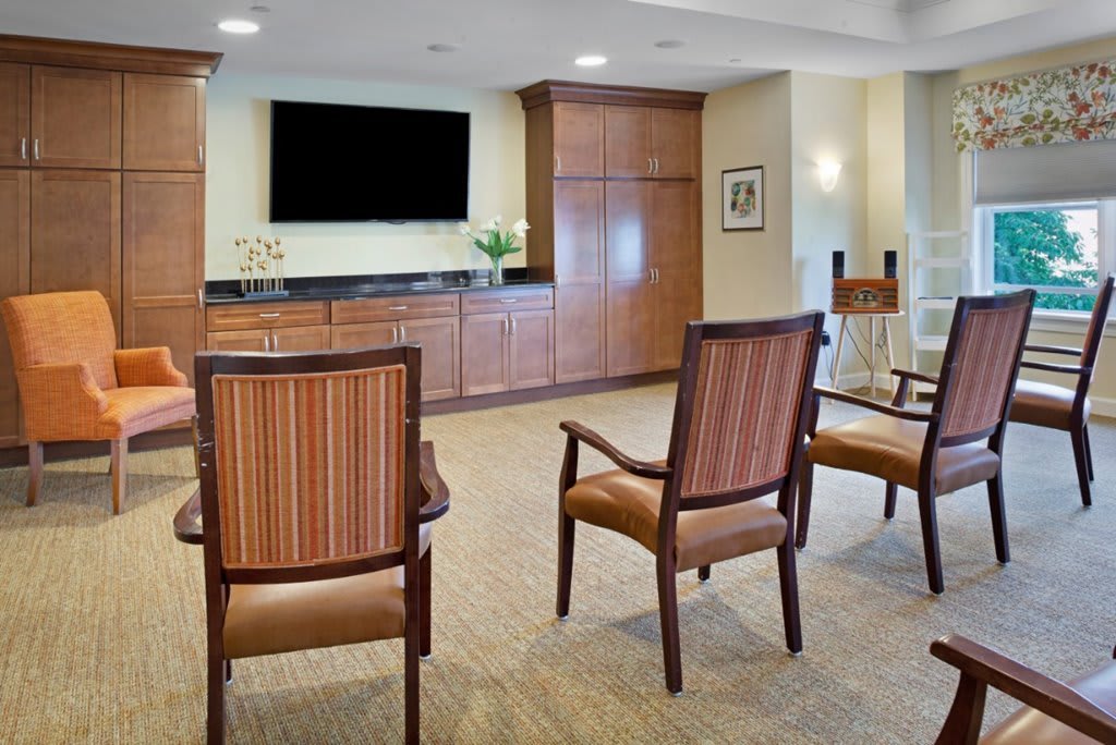 A spacious lounge area with chairs arranged facing a television and wooden cabinets.