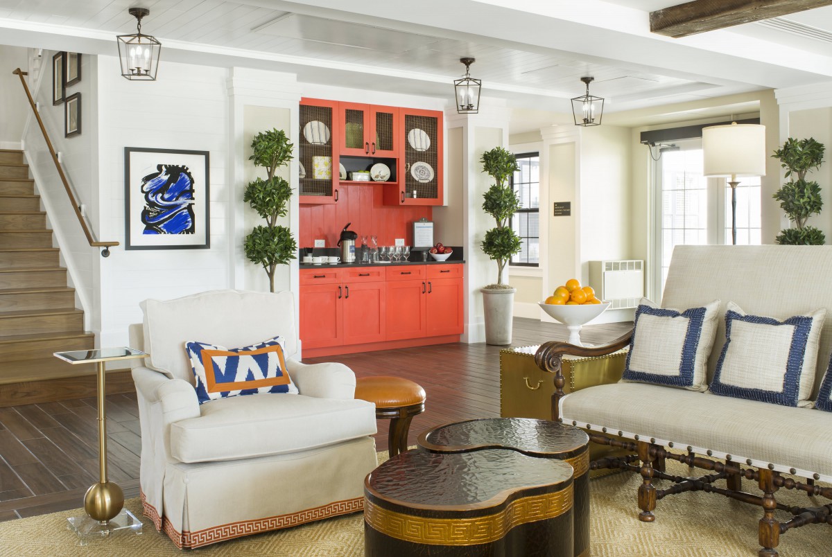 A stylish and modern living room featuring a red cabinet, comfortable armchairs, and unique wooden tables, accented by greenery.