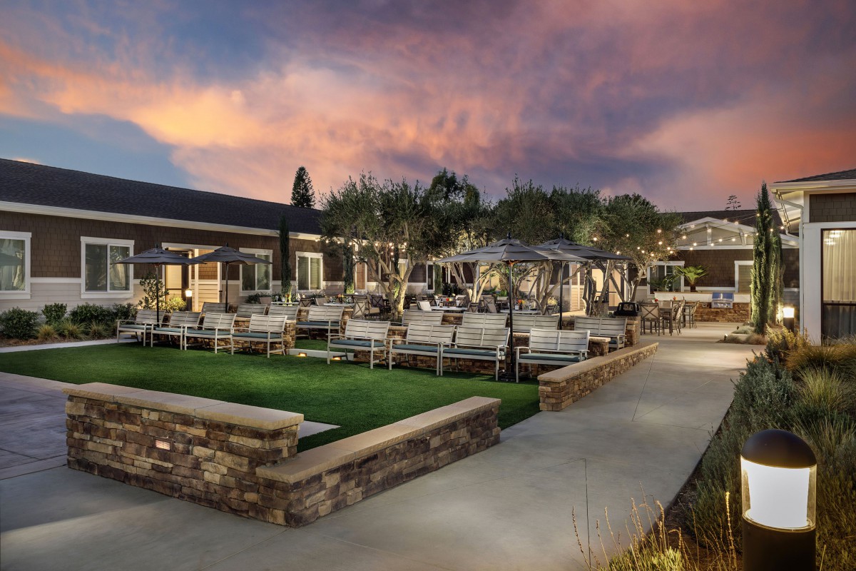 A scenic outdoor patio area with seating, illuminated by lights against a sunset backdrop.