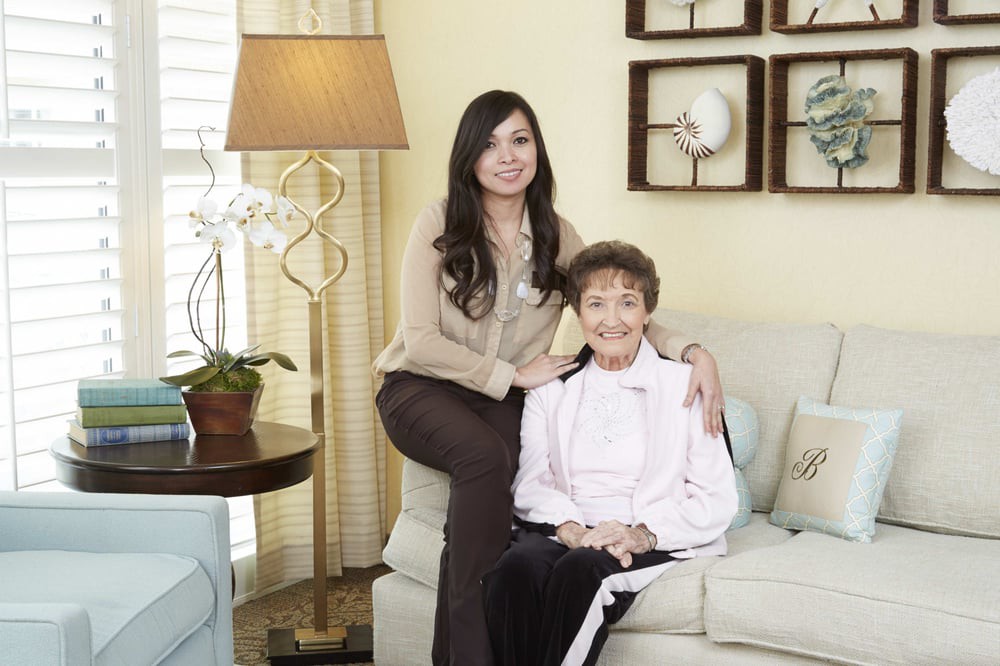 A woman sits with an older lady in a cozy living room setting.