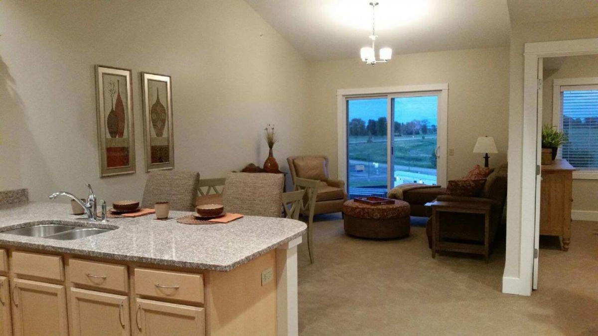 A cozy, modern living room with a kitchen counter and natural lighting from large windows.