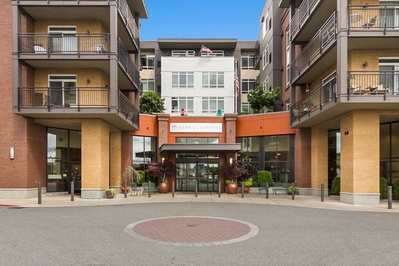 Front view of a modern apartment complex entrance with balconies and greenery.
