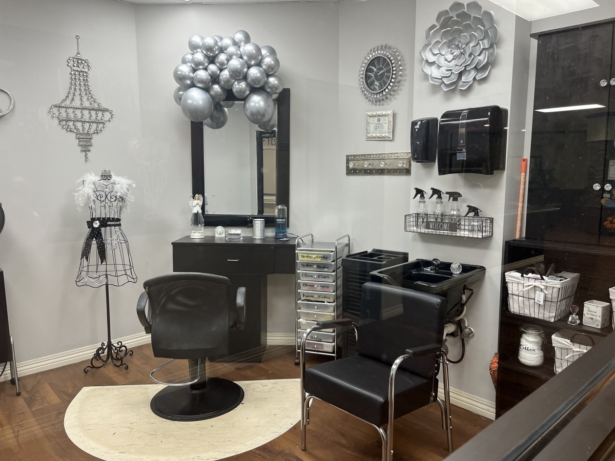 A stylish hair salon interior with a black styling chair, mirror, and silver balloon decorations.