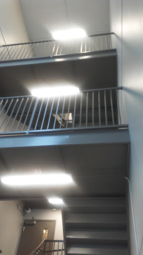 A view of an interior staircase with a balcony and overhead lighting.