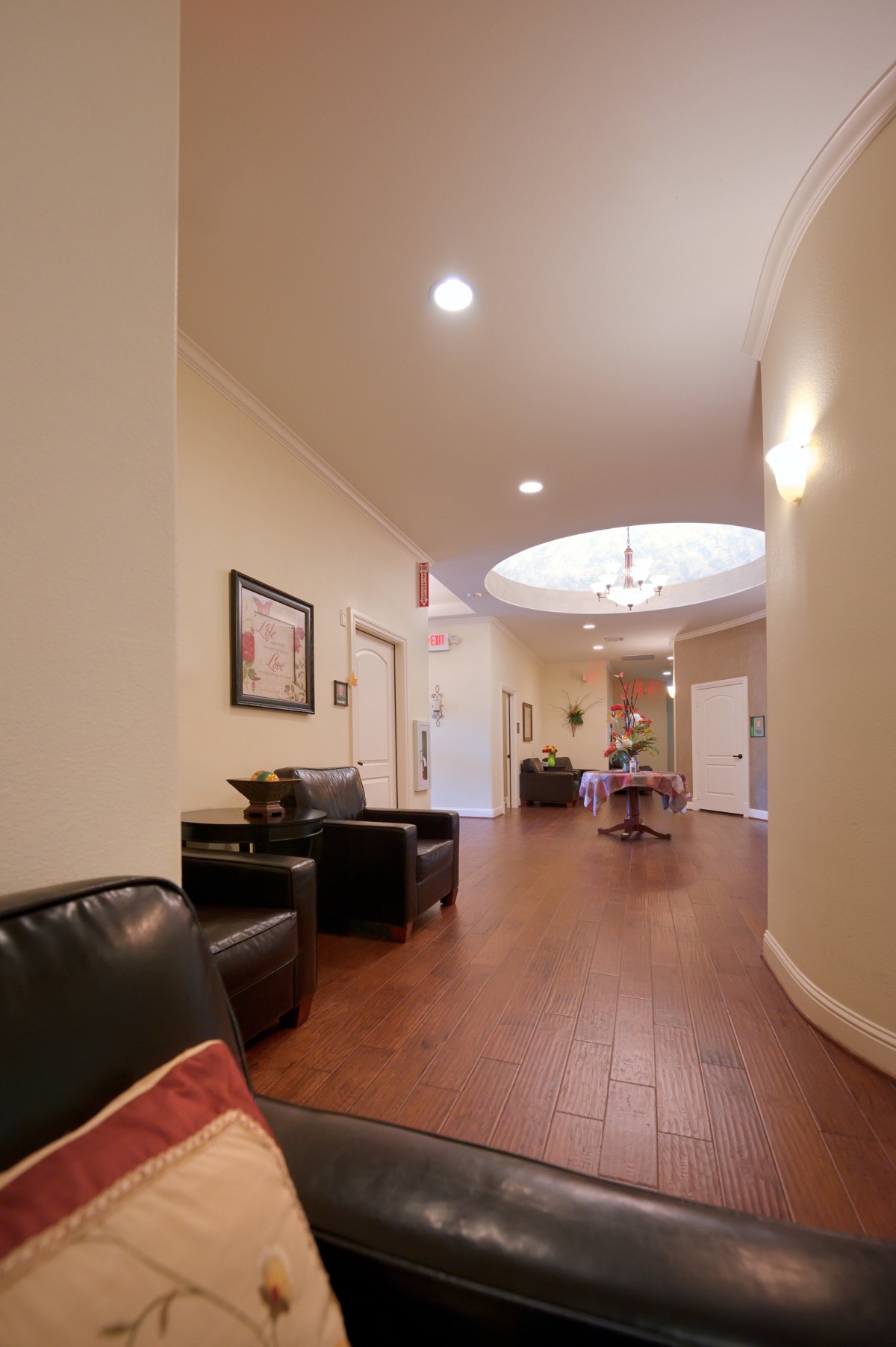 A well-lit hallway with wooden flooring, featuring a seating area and decorative artwork.