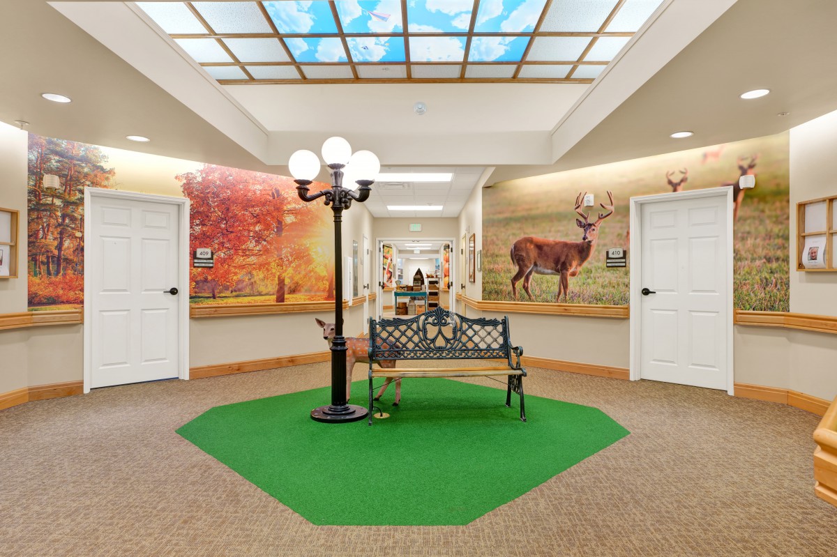 A decorated indoor hallway with a bench and light post, featuring murals of nature scenes on the walls.